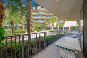 Ein Balkon mit Blick auf ein mehrgeschossiges Gebäude, Palmen und einen Poolbereich.