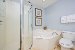 A bathroom with a glass-enclosed shower, a bathtub, and a toilet. There are two framed pictures on the wall.