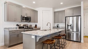 A modern kitchen with grey cabinets, stainless steel appliances, a marble countertop, and wooden bar stools.