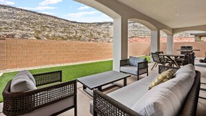 An outdoor patio with wicker furniture, a barbecue area, and a view of a hilly landscape.