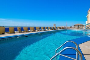 A swimming pool with lounge chairs, a lifeguard stand, and a building in the background.