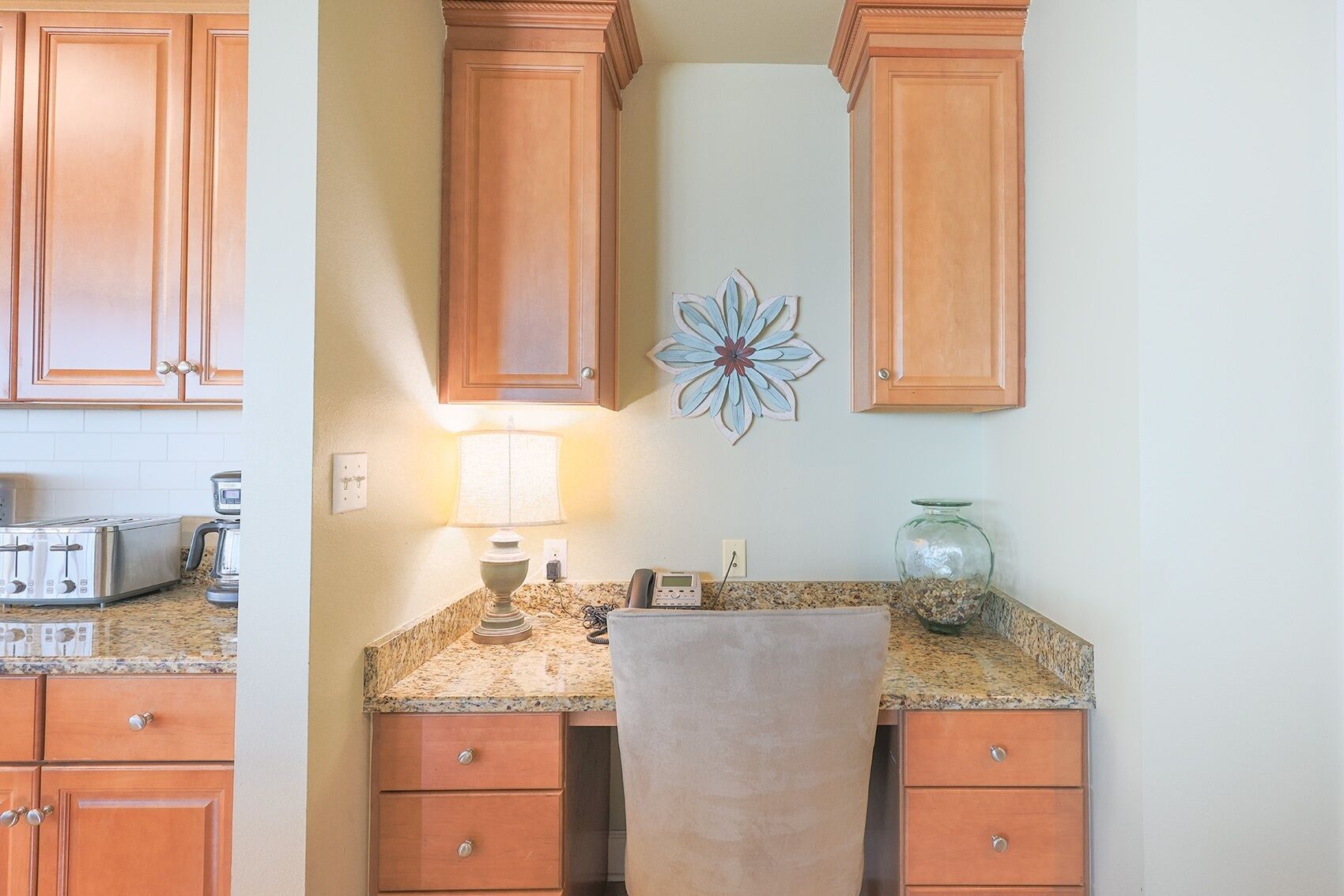 A kitchen with wooden cabinets, granite countertops, a coffee maker, a toaster, and a decorative wall piece.