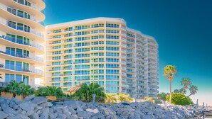 Un hôtel à plusieurs étages doté de balcons, situé sur une côte rocheuse et bordé de palmiers.