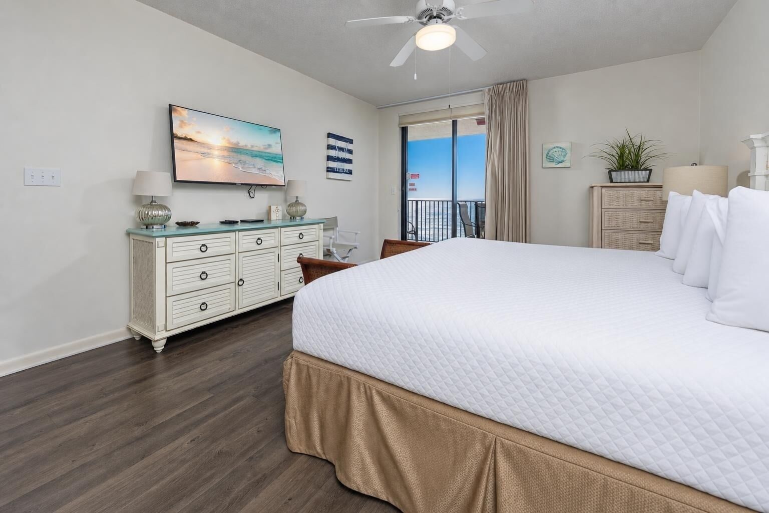 Ein Hotelzimmer mit einem Bett, einem Schminktisch, einem Deckenventilator, einem Fernseher und Blick aufs Meer.