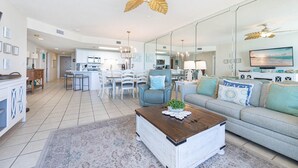 A spacious living room with a large sofa, a coffee table, and a dining area with chairs and a table. - Phoenix X 709 3 Bedroom Condo (Orange Beach)