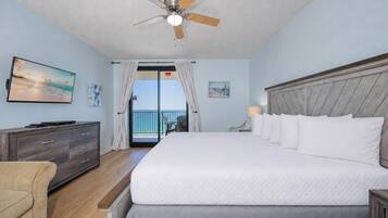 A hotel room with a bed, a ceiling fan, a TV, a dresser, and a view of the ocean.