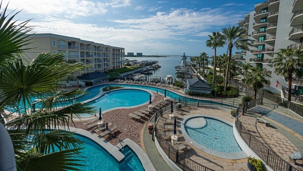 Un resort con varias piscinas, palmeras y un puerto deportivo.