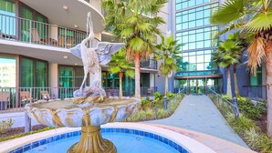 Una fuente con una escultura de pájaro en un patio rodeado de palmeras y un edificio moderno con balcones.