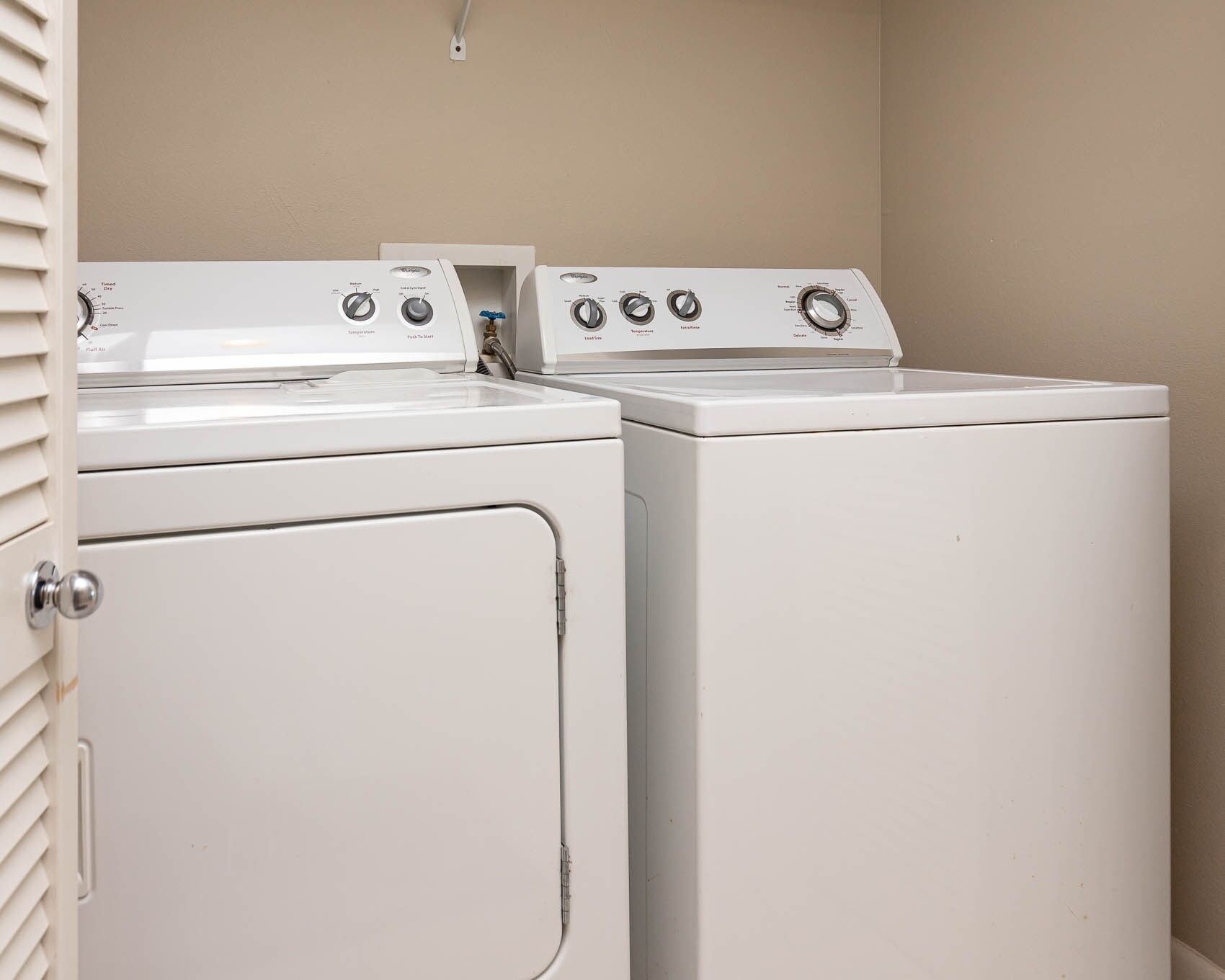 A laundry room with two stacked washers and dryers, a white door, and a light switch on the wall.