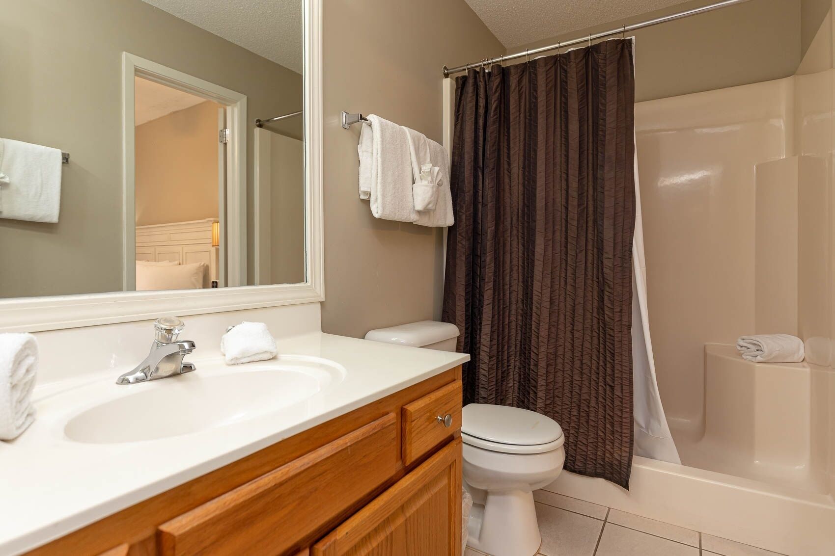 A bathroom with a white sink, wooden vanity, a mirror, a toilet, and a shower with a dark curtain.