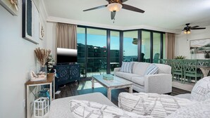 Un soggiorno moderno con divano, tavolino e televisore su un mobile. C'è un balcone con vista sugli edifici.