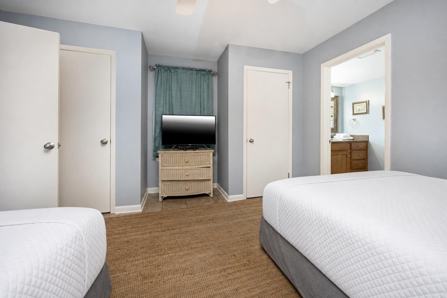 A hotel room with two beds, a TV on a dresser, and a bathroom visible through an open door.