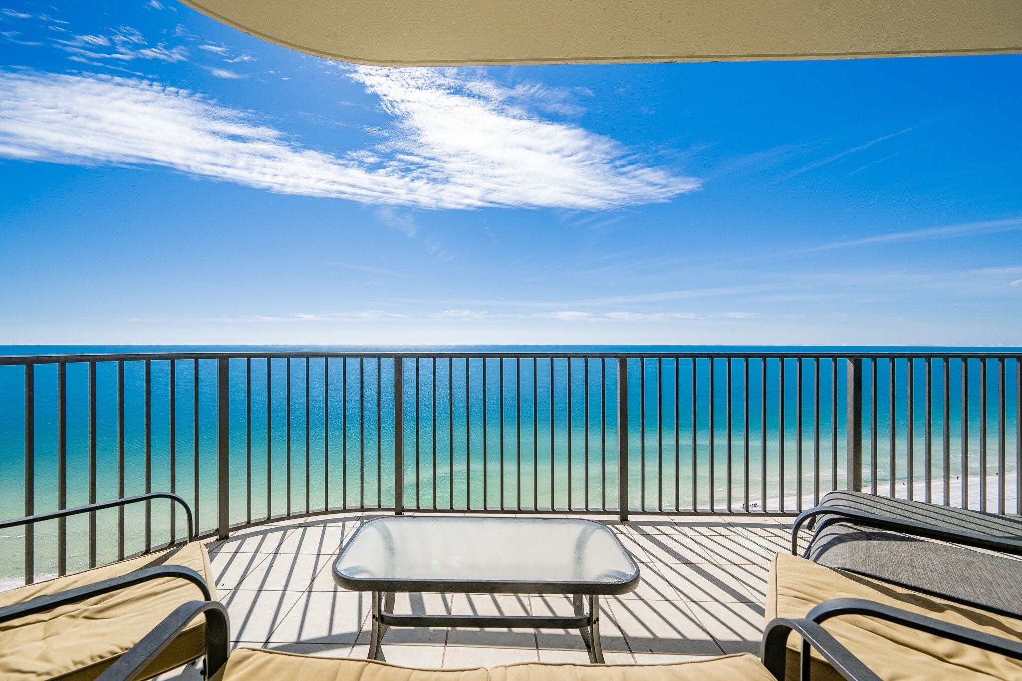 A balcony with a view of the ocean, a table, and two chairs.