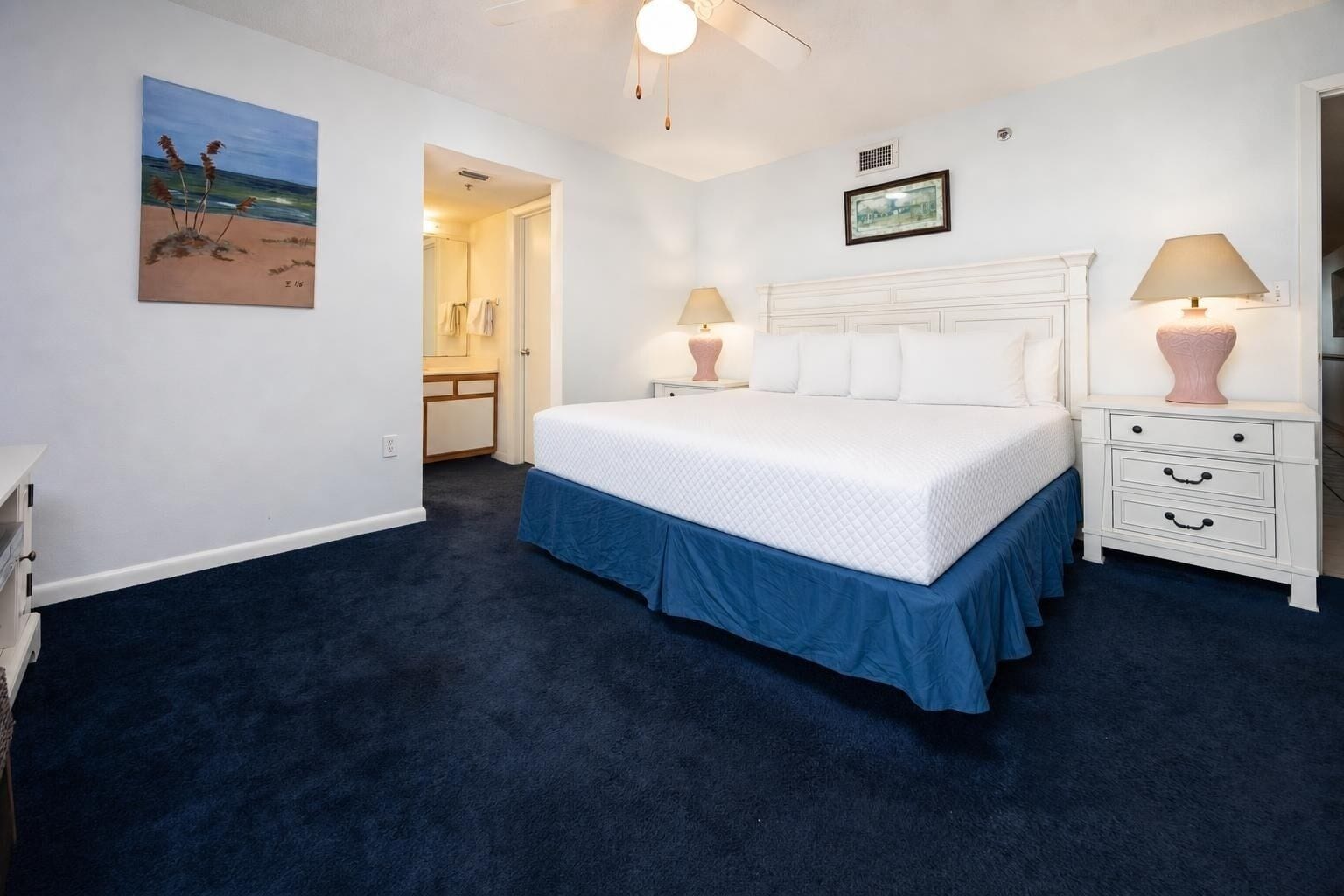 Een slaapkamer met een groot bed, nachtkastjes, een schilderij en een deur naar een andere kamer.