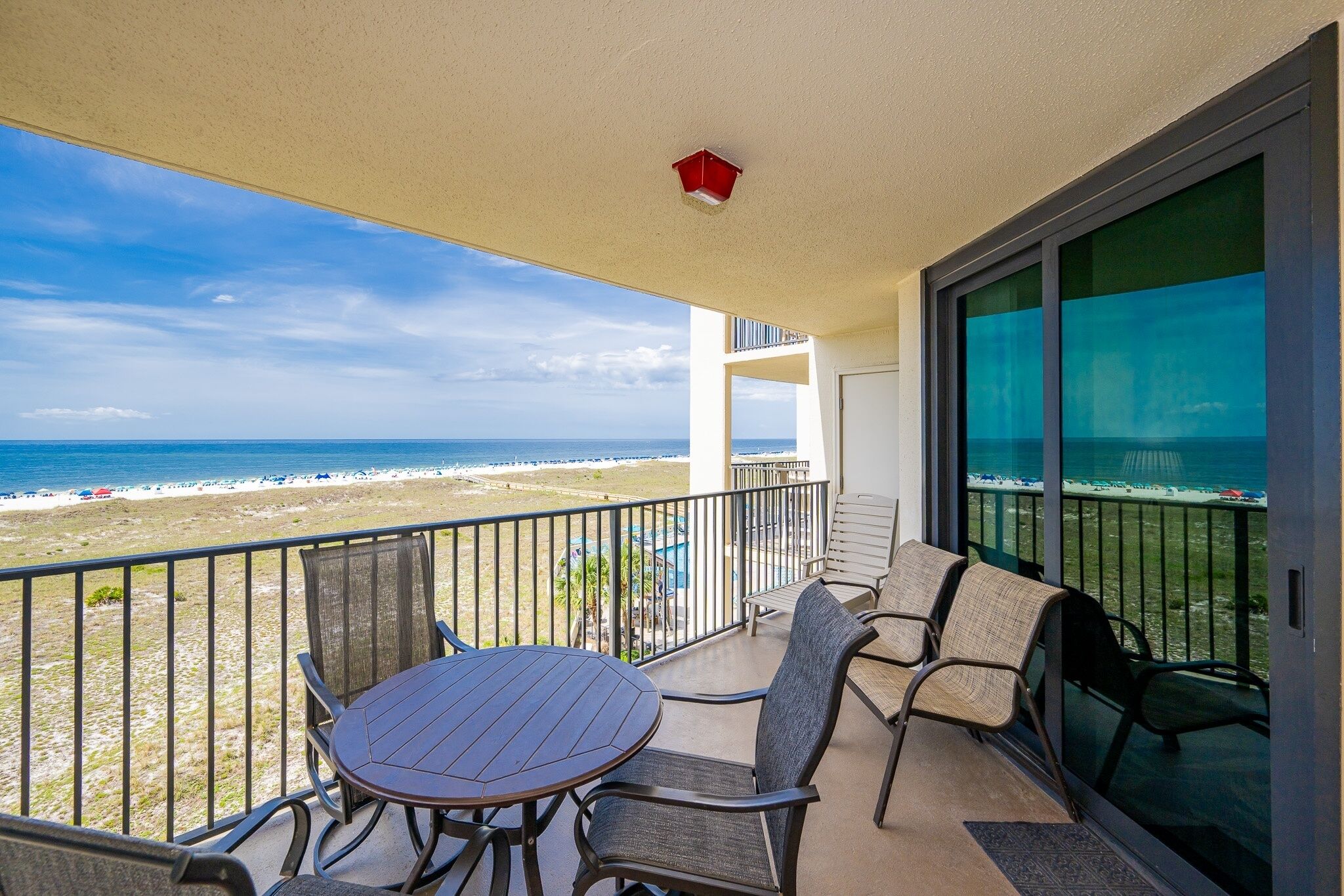 A balcony with a table and chairs, overlooking a beach with a clear view of the ocean.