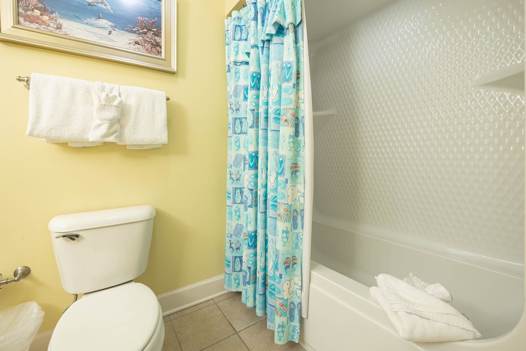 A bathroom with a toilet, a bathtub, and a shower curtain with a nautical pattern.