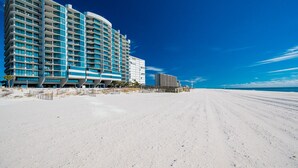 Un hôtel en bord de mer, avec plusieurs étages, une plage de sable en premier plan et un ciel bleu dégagé.