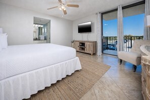Une chambre dotée d’un grand lit, d’un ventilateur de plafond, d’un téléviseur à écran plat, d’un balcon avec vue et d’un fauteuil.