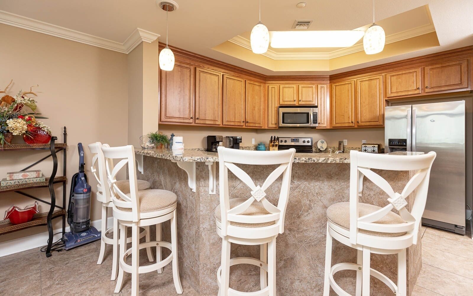A kitchen with wooden cabinets, a microwave, a refrigerator, and three white chairs.