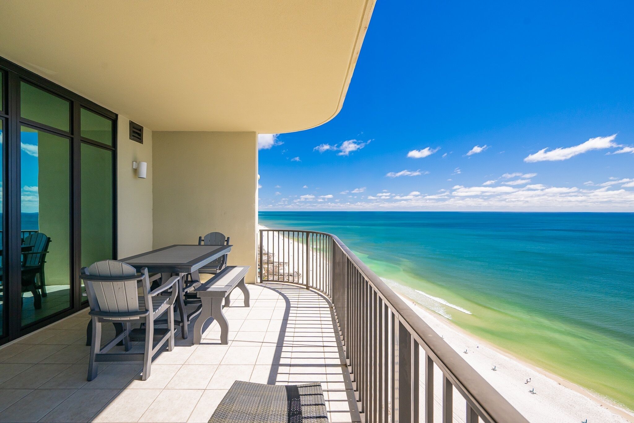 A balcony with a view of the ocean, a table, chairs, and a bench.