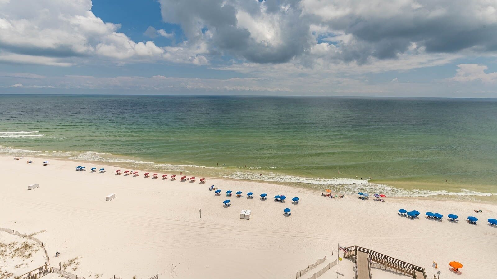 A beach with rows of sunbeds and umbrellas, a sandy shore, and the ocean in the background.