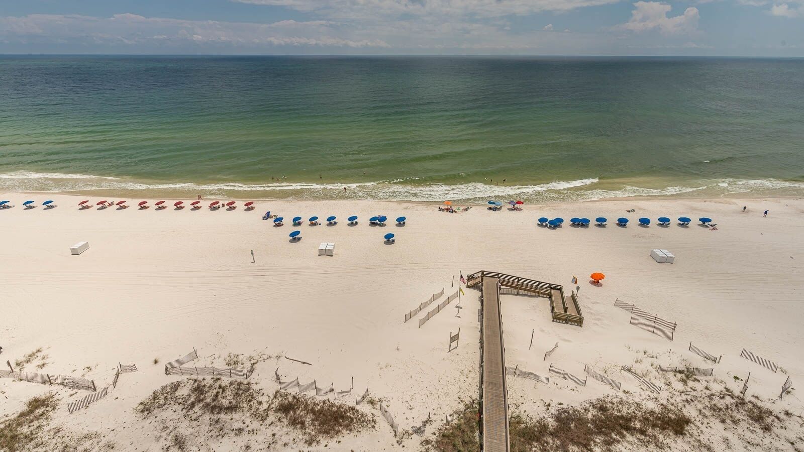 A beach with rows of umbrellas and beach chairs, a wooden boardwalk, and a sandy shoreline.