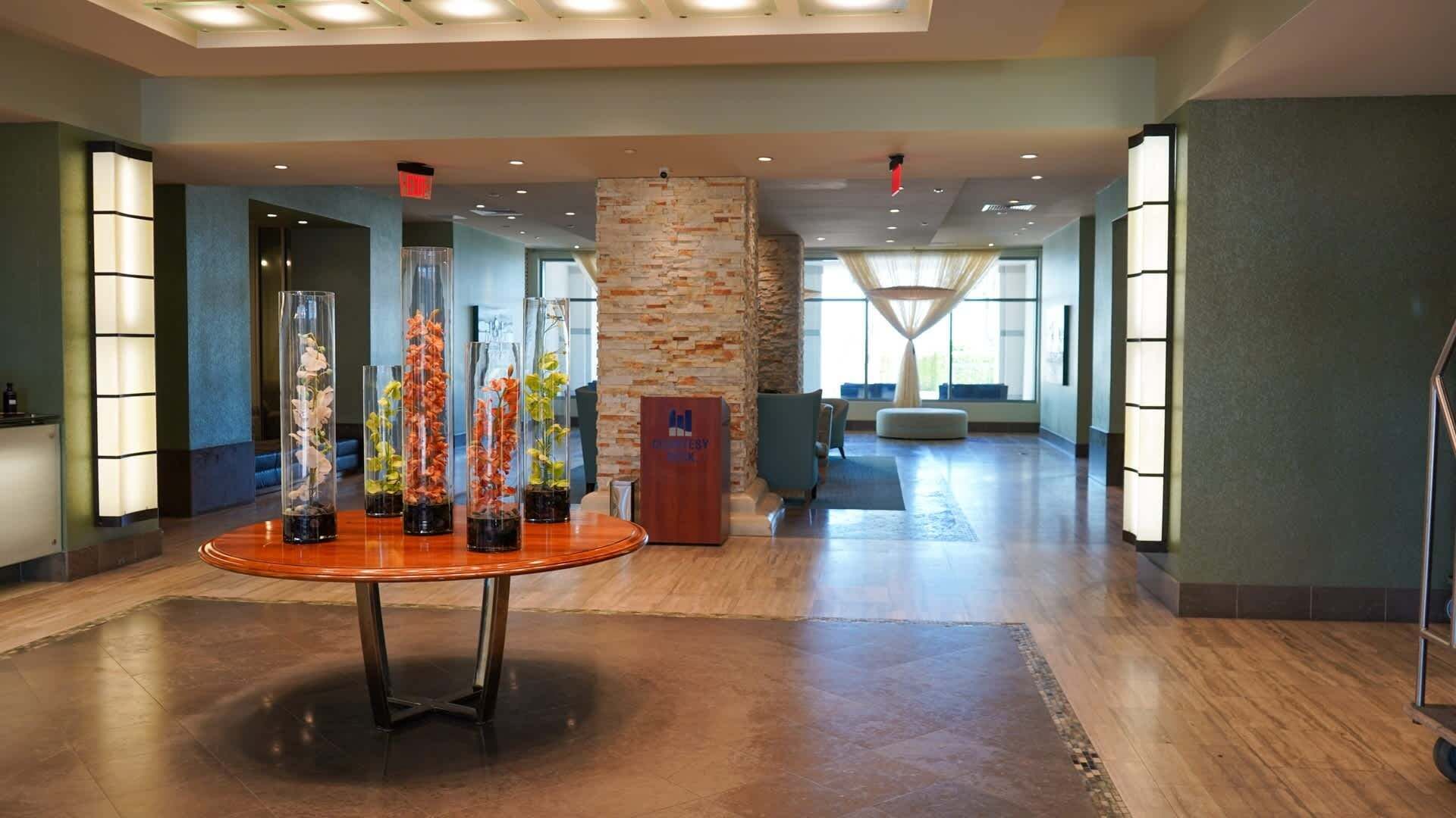 Een moderne lobby met een ronde centrale tafel waarop bloemstukken staan, een stenen pilaar en een receptiebalie.