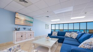 A room with a large window, a blue sofa, a white coffee table, and a cabinet with a painting. - Phoenix Iv 4023 3 Bedroom Condo (Orange Beach)