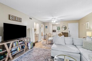 A living room with a TV, bookshelves, a white sofa, and a dining area with chairs and a table.