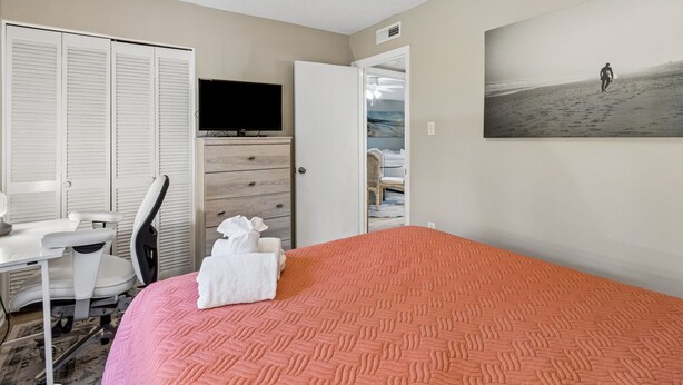 A hotel room with a bed, a desk, a chair, a television, a wardrobe, and a beach-themed painting. - 5d Amelia Landings 2 Bedroom Condo by RedAwning (Fernandina Beach)