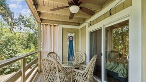 A covered porch with wicker chairs, a ceiling fan, and a glass door leading to a bedroom. - 5d Amelia Landings 2 Bedroom Condo by RedAwning (Fernandina Beach)