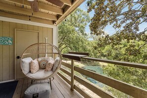 A wooden deck with a wicker chair and cushions, overlooking a natural landscape with trees and a body of water. - 5d Amelia Landings 2 Bedroom Condo by RedAwning (Fernandina Beach)