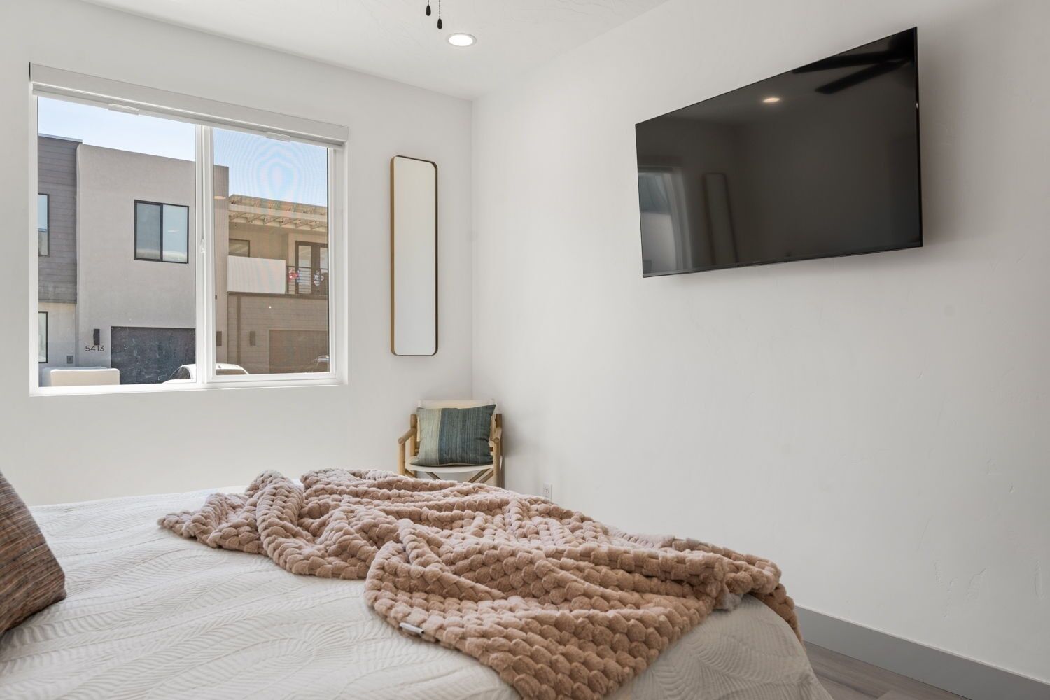 A bedroom with a bed, a large window, a chair, and a TV mounted on the wall.