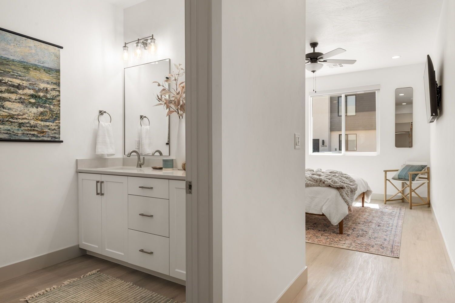 Une salle de bain moderne avec un grand miroir, un lavabo et un meuble. Il y a un tableau accroché au mur et une plante placée à côté du miroir.