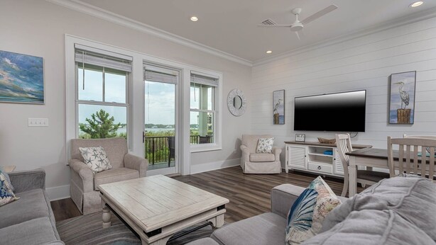 A spacious living room with a large TV, comfortable seating, and a balcony with a view. - West Side Cottages N 3 Bedroom Home (Gulf Shores)
