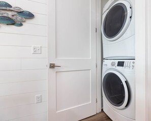 Un cuarto de lavado con dos lavadoras de carga frontal apiladas, una puerta blanca y un zapatero montado en la pared.