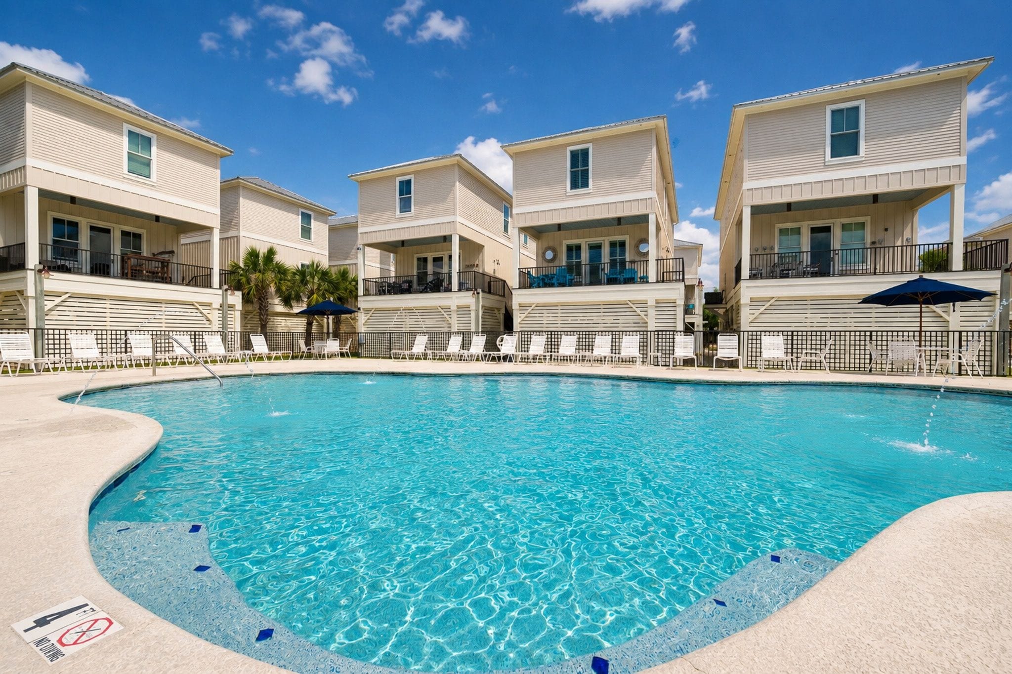A swimming pool surrounded by multi-story buildings with balconies, clear skies, and no visible people.