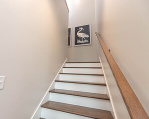 Una escalera de madera con barandilla blanca que conduce a un rellano con dos obras de arte enmarcadas.