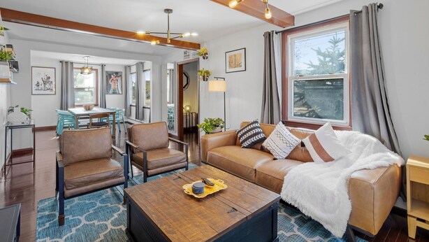 Ein modernes Wohnzimmer mit einem braunen Ledersofa, zwei Sesseln, einem Holztisch und einem Essbereich mit Tisch und Stühlen.