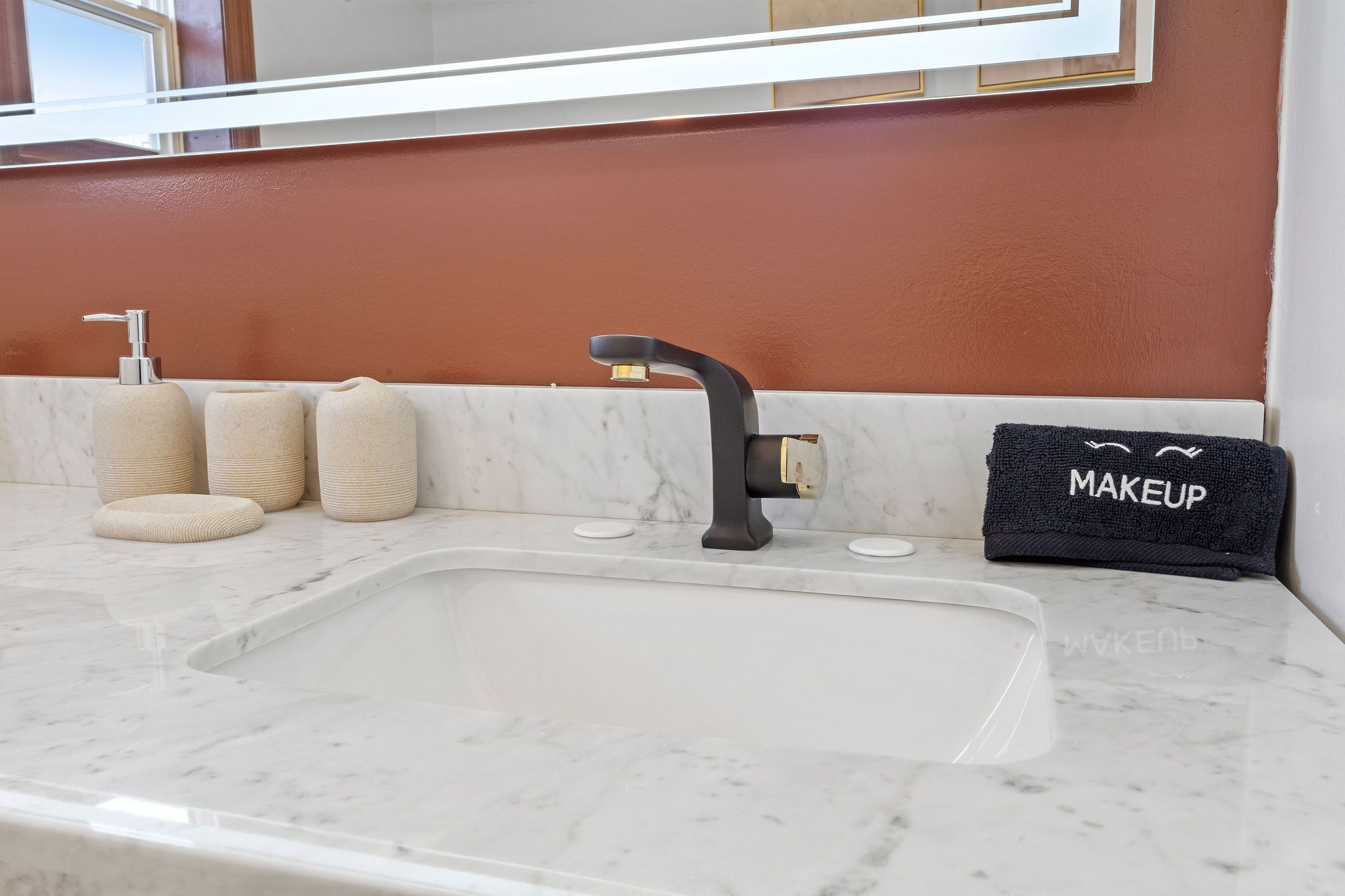 A bathroom with a marble sink, a black faucet, and a towel rack with a towel labeled "MAKEUP".