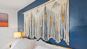 Ein Bett mit weißer Bettwäsche, ein Wandbehang aus Makramee und eine Lampe auf einem Nachttisch.
