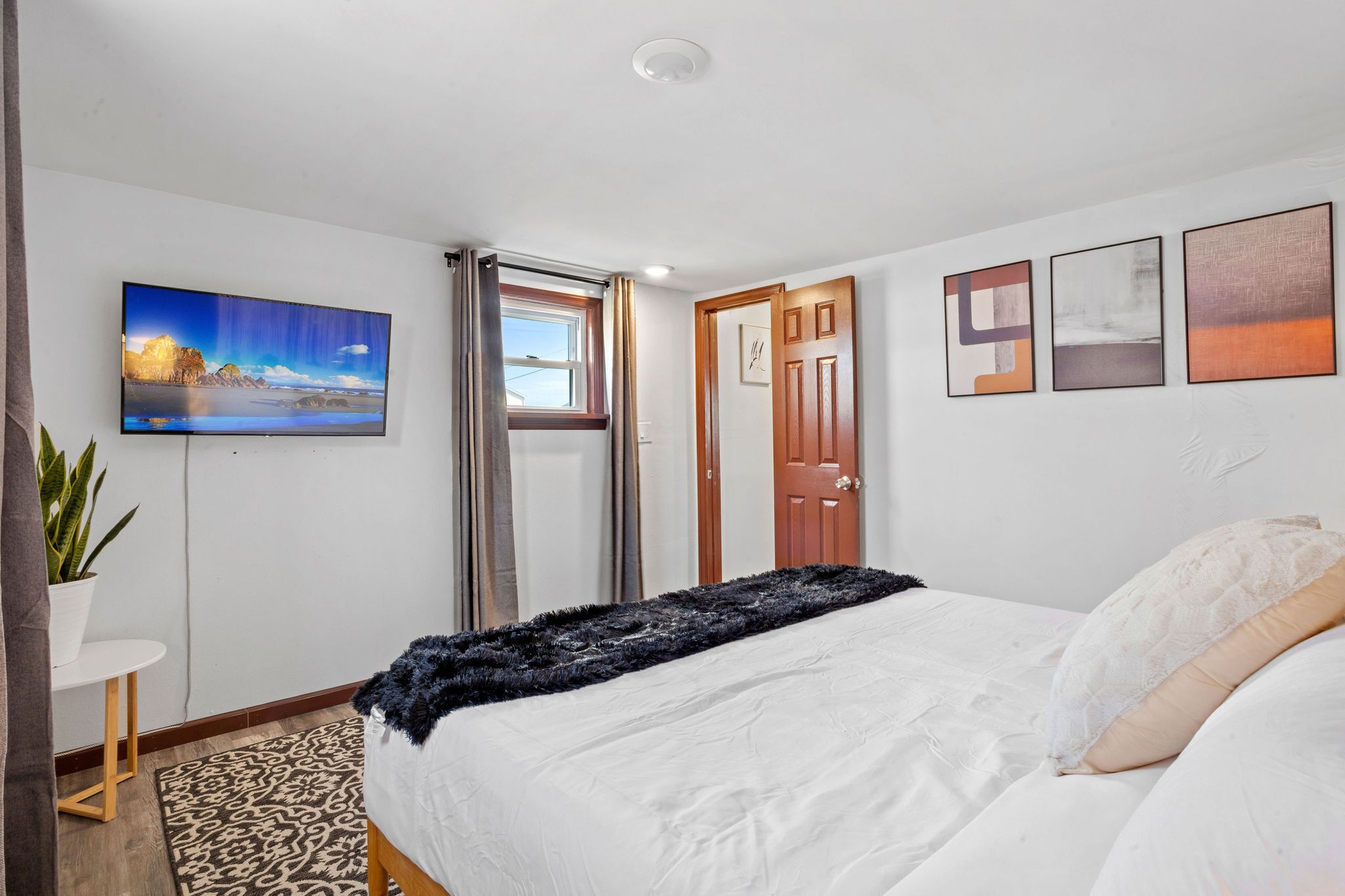 A bedroom with a bed, a TV, a door, and a window.