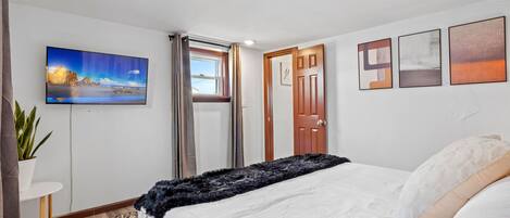 A bedroom with a bed, a TV, a door, and a window.