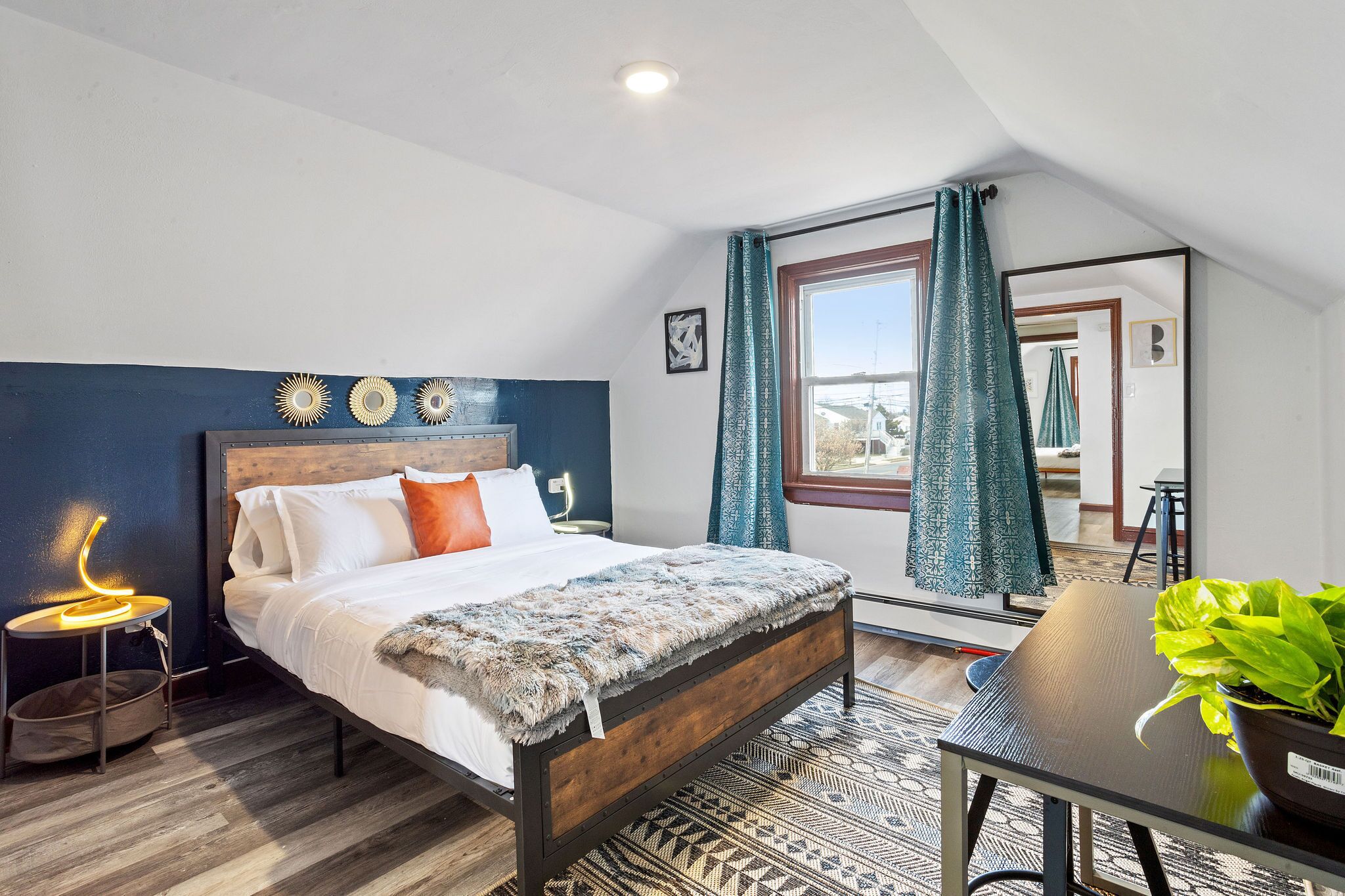 A bedroom with a bed, a bedside table with a lamp, a window with curtains, and a view of the outside.