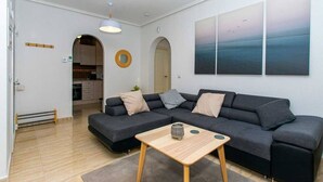 A modern living room with a sectional sofa, a small wooden coffee table, and a view of the kitchen through an archway. - CH Casa Clementina Rojales (Rojales)