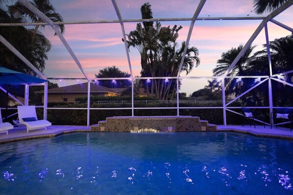 An outdoor swimming pool with a covered area, lounge chairs, and string lights.