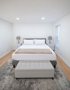A bedroom with a bed, bedside tables, and a window with blinds.