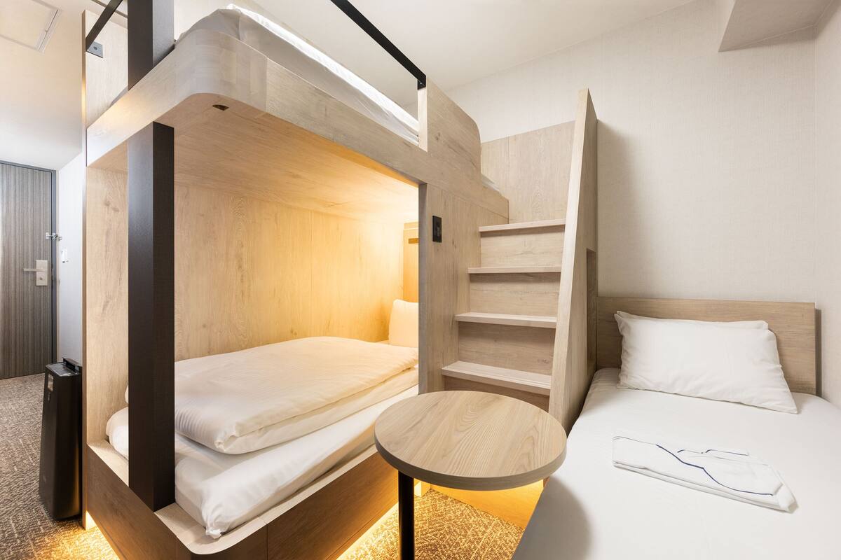 A bunk bed room with a small table and a single bed.