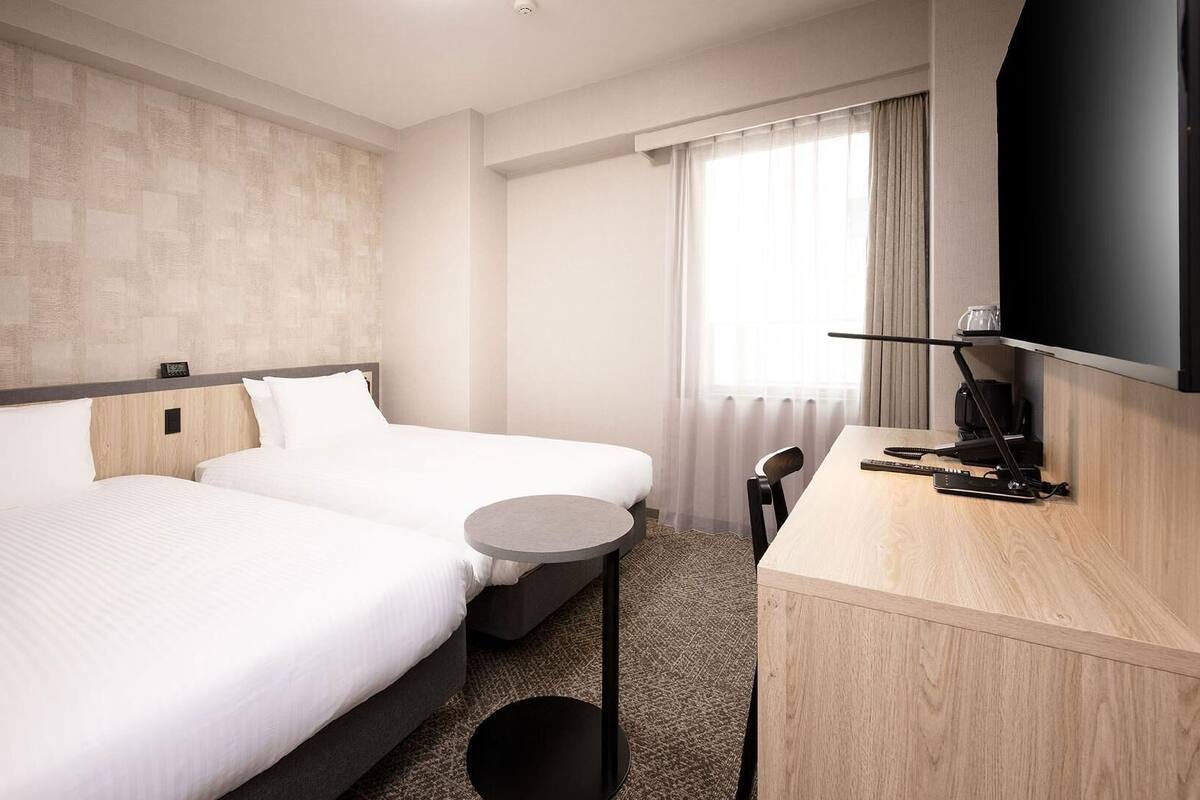 A hotel room with two beds, a small round table, a TV, and a desk with a chair.