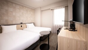 Habitación de hotel con dos camas, una mesita redonda pequeña, un escritorio con televisor de pantalla plana y una ventana con cortinas.